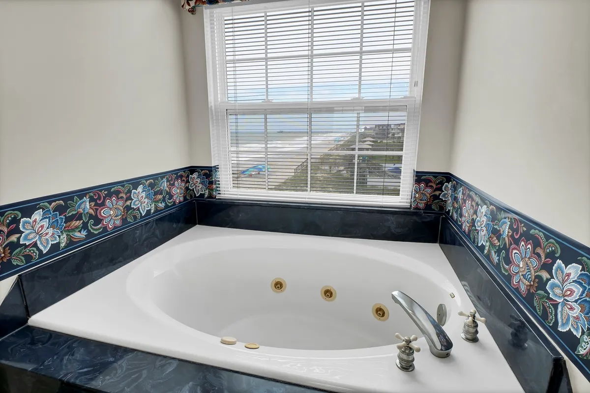 A serene bathroom with a jacuzzi bathtub, decorative tile border, and a window overlooking scenic views. The space is bright and inviting, ideal for luxurious self-care and quiet moments.