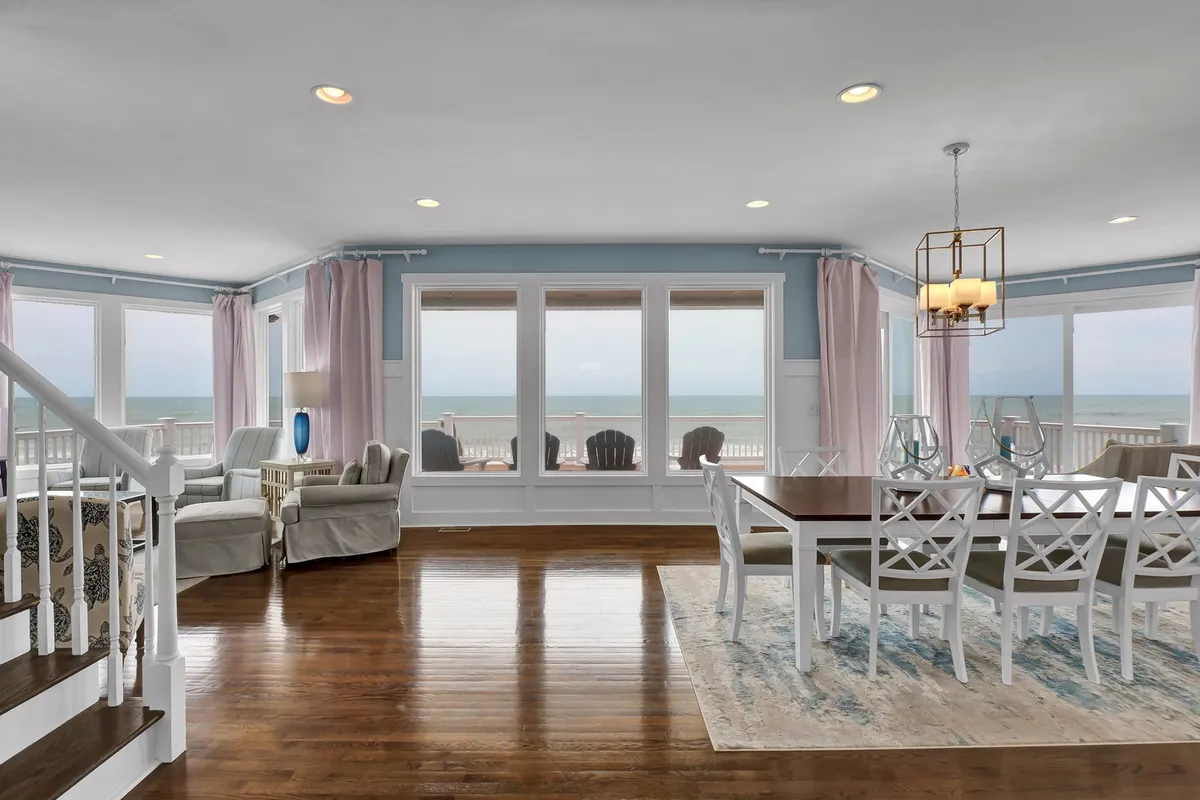 This image showcases a spacious, open-concept living and dining area featuring large windows that frame sweeping ocean views. The comfortable seating area and dining table are positioned to take full advantage of the natural light and seaside scenery, inviting relaxation, conversation, and shared meals with the ocean as a backdrop.