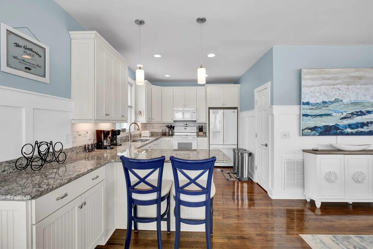 A modern kitchen with granite countertops, a spacious island, blue accent chairs, and contemporary appliances. The kitchen is designed for social cooking and entertaining, with sightlines open to the rest of the living area, aligning with the seamless flow described in the section.