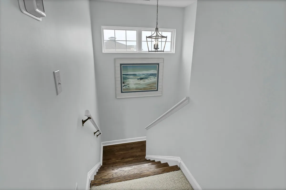 A tranquil interior view highlighting an elegant spiral staircase with a modern light fixture above and ocean-themed wall art, setting an impressive architectural centerpiece in the entryway.