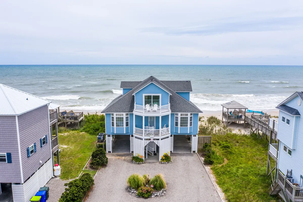 A beachfront house nestled along North Topsail Beach, with a sweeping view of the ocean and well-kept landscaping in the foreground. The image captures the immediate proximity of the home to the sandy shoreline, creating a direct connection to the beach. The relaxed setting suggests ample opportunity for outdoor activities and gatherings.