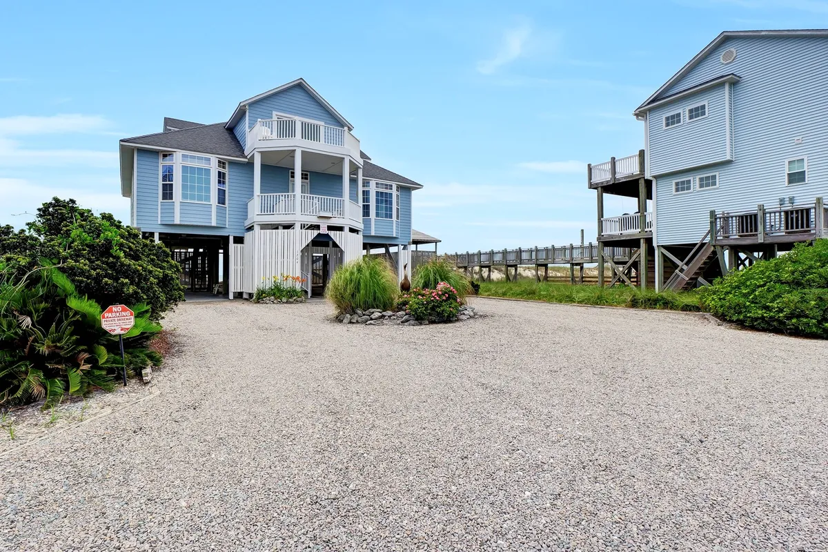 An exterior shot of the main house with a landscaped garden and gravel driveway, exuding a welcoming and serene mood. The space hints at outdoor relaxation and offers a sense of arrival for group guests.